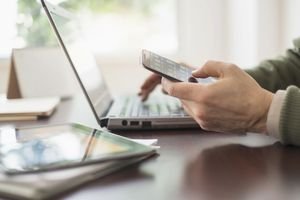 Close up of mans hands working at desk with electronic devices