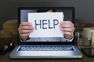 Photo of a man holding a HELP sign through a laptop screen
