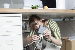 Young woman crouching under a desk connecting a modem in an office