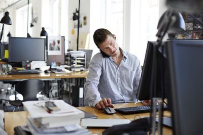 Photo of a man talking on the phone while using a computer