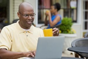 Black man using laptop at sidewalk cafe