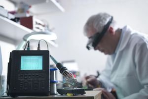 Engineer soldering prototype circuit board with oscilloscope in foreground