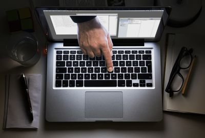 Hand appearing from laptop screen touches keyboard