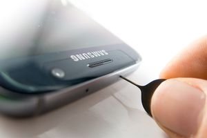 A close up of a Samsung phone with fingers using a tool to open the SIM card slot.