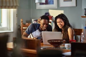 Couple laughing at footage on laptop at breakfast
