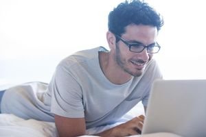 Smiling man using laptop in bed