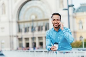 20-something Latino male using prepaid cell phone with city background.
