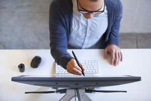 A picture of a man drawing on a computer screen with a stylus.