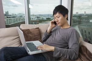 Asian mid adult man on call while using laptop in living room