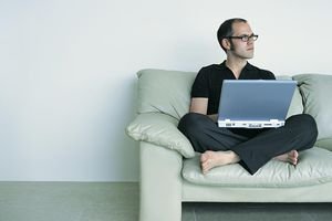 Man Looking Away Sitting Cross Legged on a Sofa Using a Laptop