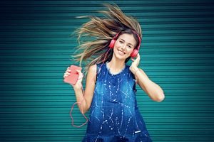 A young girl dancing to music while wearing red headphones plugged into a smartphone